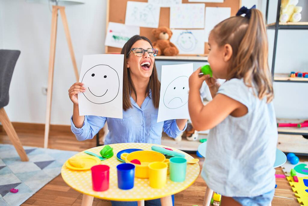 Młoda terapeutka mówiąca i lecząca dzieci, wychowawczyni i korygująca zachowanie w pokoju płac pedagogicznych z radosnymi i smutnymi twarzami - Zdjęcie, obraz