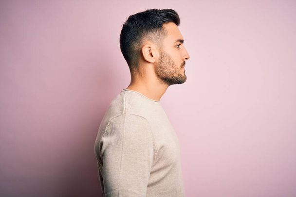 Young handsome man wearing casual sweater standing over isolated pink background looking to side, relax profile pose with natural face with confident smile. - Foto, Imagem