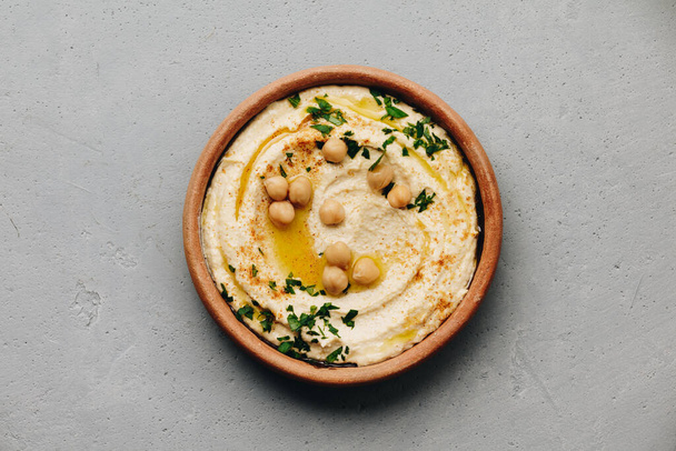 Large bowl of homemade hummus garnished with chickpeas, red sweet pepper, parsley and olive oil - Foto, afbeelding