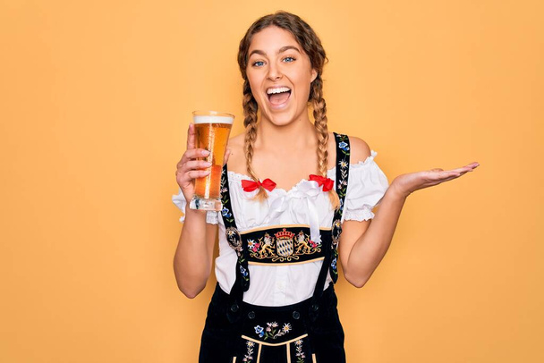 Прекрасна блондинка-германка з блакитними очима в октоберфест сукні, що п'є пиво дуже щасливе і збуджене, переможний вираз, що прославляє перемогу з великою посмішкою і піднятими руками. - Фото, зображення
