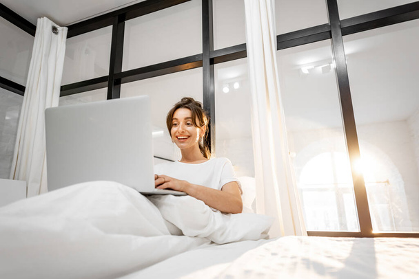 Woman with laptop at shiny bedroom - Fotoğraf, Görsel