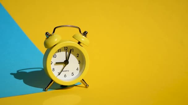 Yellow alarm clock on a yellow and blue colorful background, Deep shadows, Morning sunlight, stock footage, with numbers and a ticking arrow, The concept of time, delay, morning rise, the appointed - Footage, Video