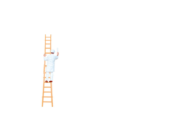 Miniature people with ladder holding brush in front of a white wall background - Photo, Image