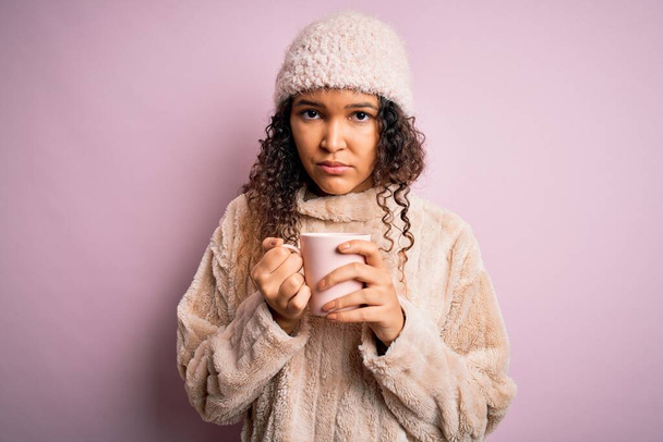 Jovem mulher bonita com cabelo encaracolado bebendo caneca de café sobre fundo rosa isolado com uma expressão confiante no rosto inteligente pensando sério
 - Foto, Imagem
