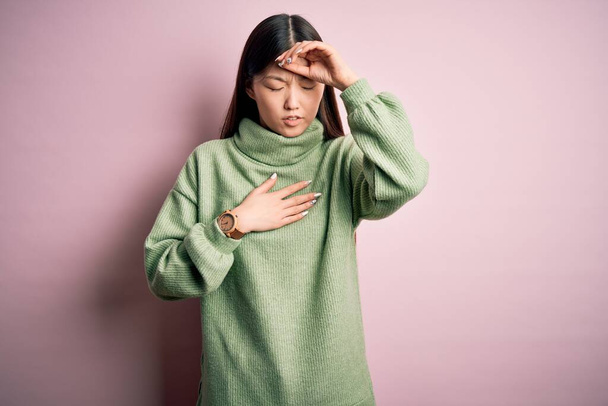 Nuori kaunis aasialainen nainen yllään vihreä talvi villapaita vaaleanpunainen eristetty tausta Koskettava otsa sairaus ja kuume, flunssa ja kylmä, virus sairas
 - Valokuva, kuva