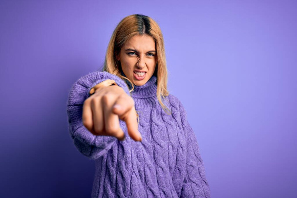 Giovane bella donna bionda indossa casual maglione dolcevita su sfondo viola che punta scontento e frustrato per la fotocamera, arrabbiato e furioso con voi
 - Foto, immagini