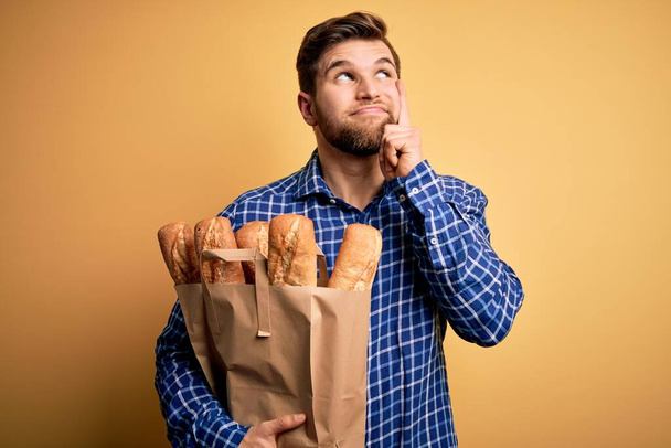 Sakallı, mavi gözlü, elinde ekmek torbası olan genç, sarışın bir adam. Ciddi bir yüz ifadesi var. Soru sormayı düşünüyor. - Fotoğraf, Görsel