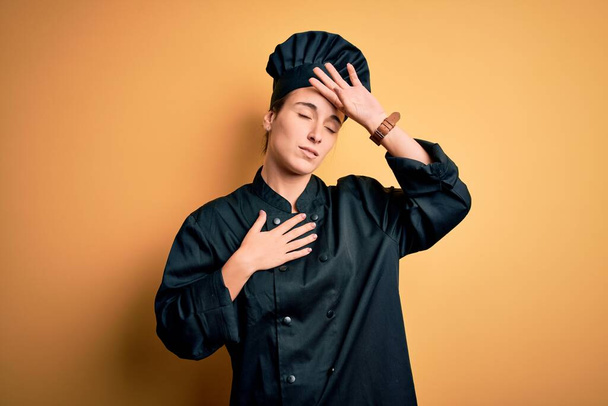 Young beautiful chef woman wearing cooker uniform and hat standing over yellow background Touching forehead for illness and fever, flu and cold, virus sick - Fotó, kép