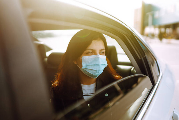 Girl in protective sterile medical mask on her face is sitting in a taxi. The concept of preventing the spread of the epidemic and treating coronavirus, pandemic in quarantine city. Healthcare concept - Fotoğraf, Görsel