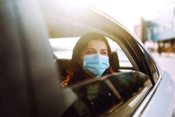 Girl in protective sterile medical mask on her face is sitting in a taxi. The concept of preventing the spread of the epidemic and treating coronavirus, pandemic in quarantine city. Healthcare concept - Φωτογραφία, εικόνα