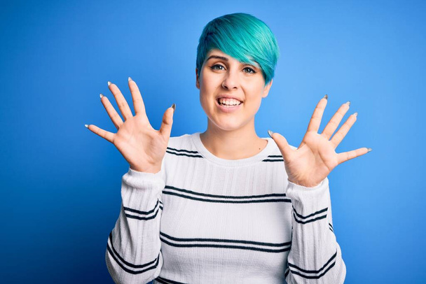 Jovem mulher bonita com cabelo azul moda vestindo camisola casual em pé no estúdio mostrando e apontando para cima com os dedos número dez enquanto sorri confiante e feliz
. - Foto, Imagem