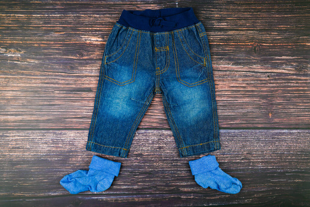 Детские джинсы на деревянном фоне. Модная концепция. Концепция одежды. Темный деревянный фон. Малыш и джинсы. Детская одежда
 - Фото, изображение