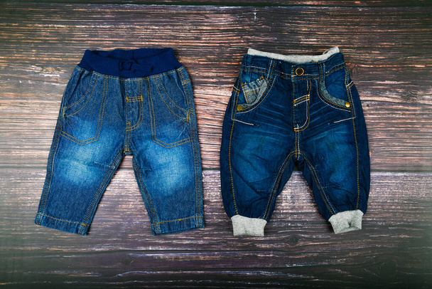 Childrens jeans on a wooden background. Fashionable concept. The concept of clothing. Dark wooden background. Baby boy and jeans. Baby Clothing - Photo, Image