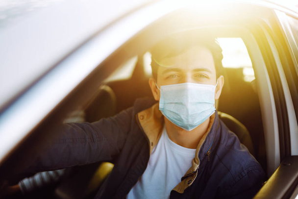 Young man in protective sterile medical mask driving car. The concept of preventing the spread of the epidemic and treating coronavirus, pandemic in quarantine city. Covid -19. - Фото, изображение