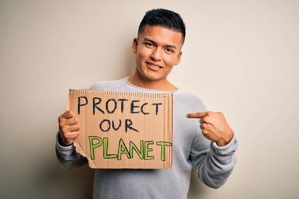 Giovane bell'attivista latino che tiene lo striscione chiedendo di proteggere il nostro pianeta con la faccia sorpresa che punta il dito verso se stesso
 - Foto, immagini