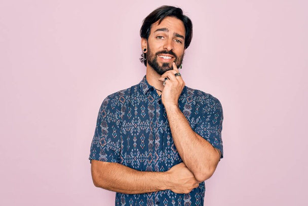 Fiatal jóképű spanyol bohém férfi hippi stílusban rózsaszín háttér néz magabiztos a kamera mosolyog keresztbe tett karokkal és felemelt kézzel áll. Pozitív gondolkodás. - Fotó, kép