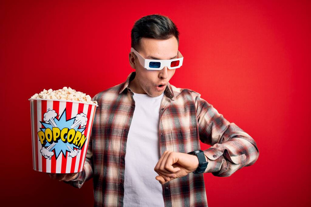 Молодий красивий кавказький чоловік одягнений в 3d кіноокуляри і їсть попкорн Дивлячись на час годинника стурбований, боїться запізнитися
 - Фото, зображення