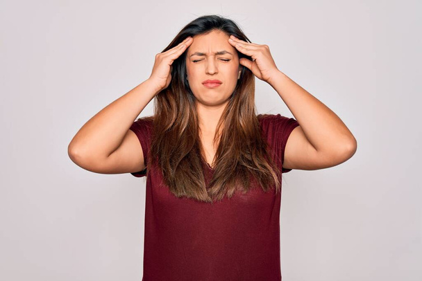 Молода іспаномовна жінка в повсякденній футболці стоїть над ізольованим тлом, страждаючи від головного болю відчайдушно і стресу, тому що біль і мігрень. Руки на голові
. - Фото, зображення