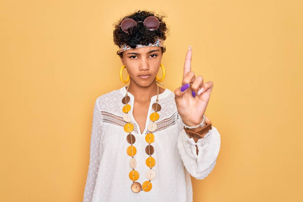 jong mooi Afrikaans amerikaans afro hippie vrouw dragen zonnebril en accessoires wijzend met vinger omhoog en boze uitdrukking, tonen geen gebaar - Foto, afbeelding