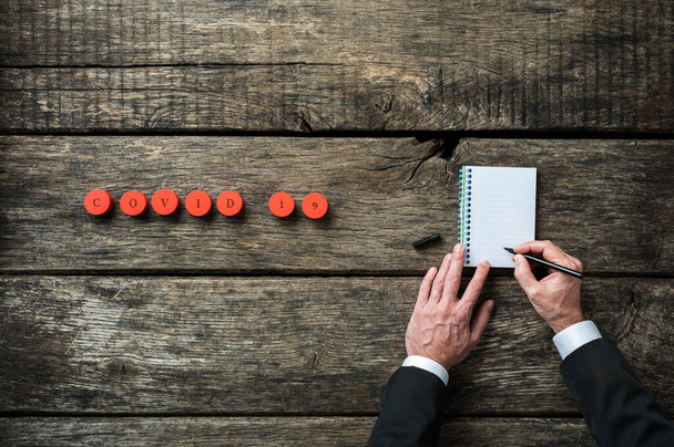 Covid 19 signe sur les cercles de coupe en bois rouge avec représentant pharmaceutique prenant des notes dans son bloc-notes. Sur fond de bois rustique
. - Photo, image