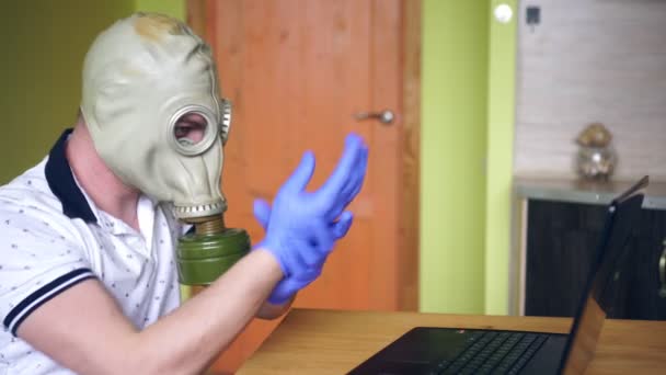 家の中にノートパソコンがあるガスマスクの男。コロナウイルス保護の概念。内務省 - 映像、動画