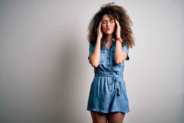 Young beautiful woman with curly hair and piercing wearing casual denim dress with hand on head for pain in head because stress. Suffering migraine. - Photo, Image
