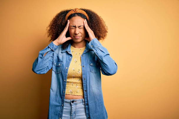 Krásný africký Američan s afro vlasy stojící nad žluté izolované pozadí trpí bolestí hlavy zoufalé a vystresované, protože bolest a migréna. Ruce za hlavu. - Fotografie, Obrázek