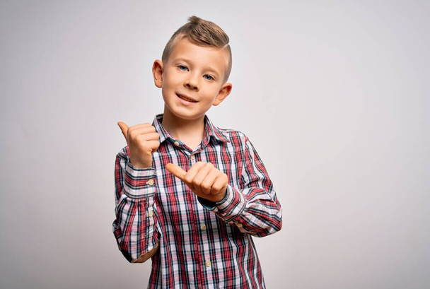 Young little caucasian kid with blue eyes wearing elegant shirt standing over isolated background Pointing to the back behind with hand and thumbs up, smiling confident - 写真・画像