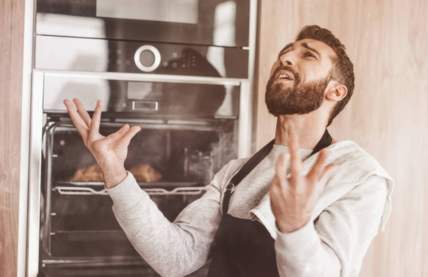 surprised man standing near the oven with burnt croissants. - Photo, Image