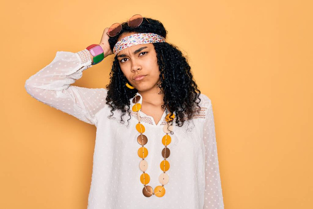 Young african american curly hippie woman wearing sunglasses and vintage accessories confuse and wonder about question. Uncertain with doubt, thinking with hand on head. Pensive concept. - Photo, Image