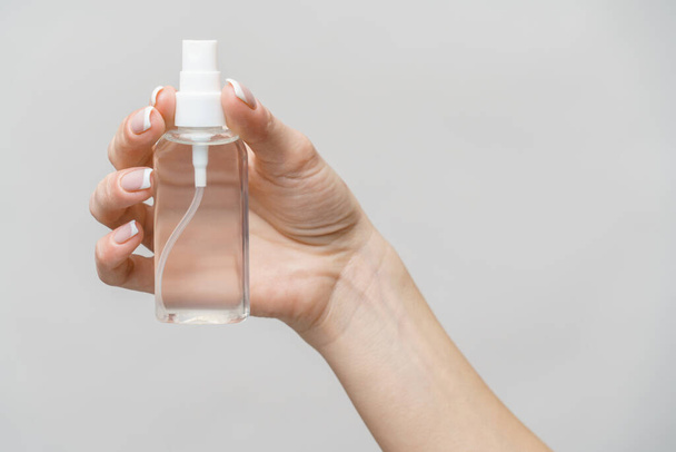 Female hands using hand sanitizer spray dispenser over light grey background - Фото, изображение