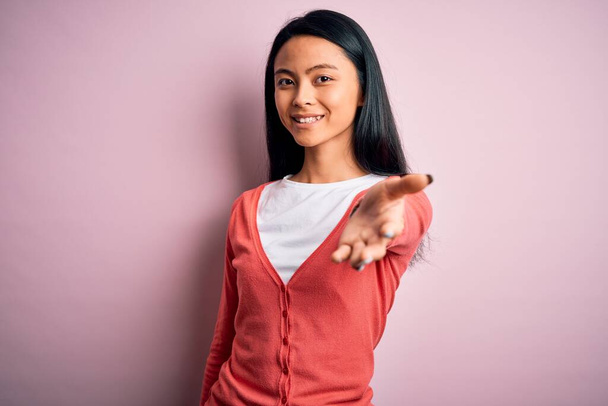 Mladý krásný číňan žena na sobě ležérní svetr přes izolované růžové pozadí s úsměvem veselá nabídka dlaně ruku dávat pomoc a přijetí. - Fotografie, Obrázek