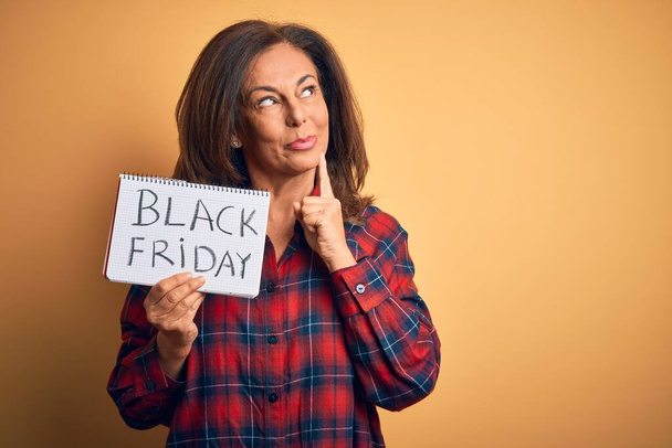 Жінка середнього віку брюнетка тримає чорне п'ятничне паперове оголошення над ізольованим тлом серйозне обличчя, думаючи про питання, дуже заплутана ідея
 - Фото, зображення