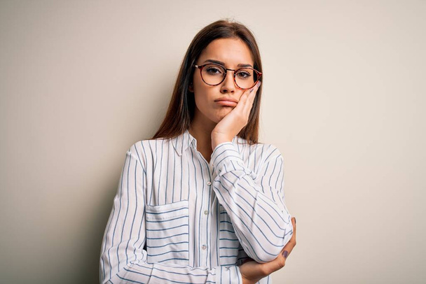 Young beautiful brunette woman wearing casual shirt and glasses over white background thinking looking tired and bored with depression problems with crossed arms. - Valokuva, kuva