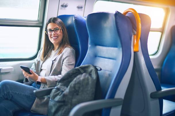 Young beautiful woman smiling happy and confident. Sitting with smile on face using smartphone travelling by train - Photo, Image