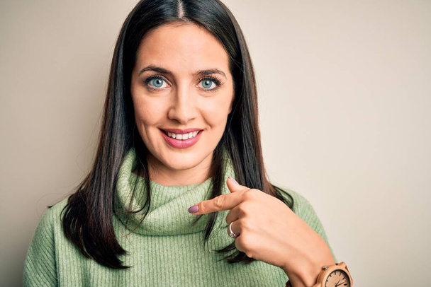 Young brunette woman with blue eyes wearing turtleneck sweater over white background with surprise face pointing finger to himself - Foto, Imagen