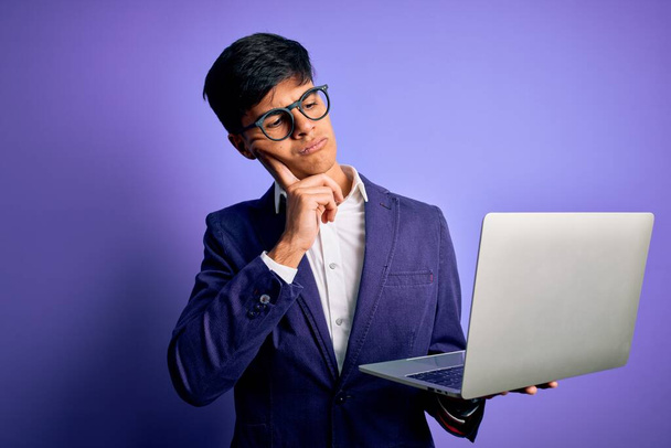 若いですハンサムなビジネス男を着て眼鏡を使用して作業ノートパソコン上で紫の背景深刻な顔を考えて質問については、非常に混乱したアイデア - 写真・画像