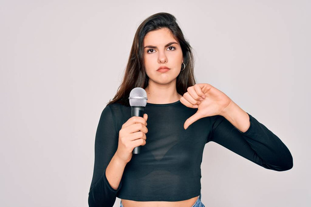 Молодая красивая певица, поющая с помощью музыкального микрофона на изолированном фоне с сердитым лицом, негативный знак, показывающий неприязнь с опущенными пальцами, концепция отказа
 - Фото, изображение