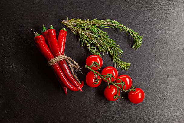 Red chili peppers, rosemary, tomatoes cherry served on black schist surface - Fotoğraf, Görsel