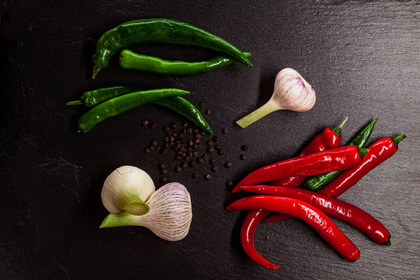 Green and red chili peppers, black peppercorns and garlic placed on schist surface - Foto, immagini