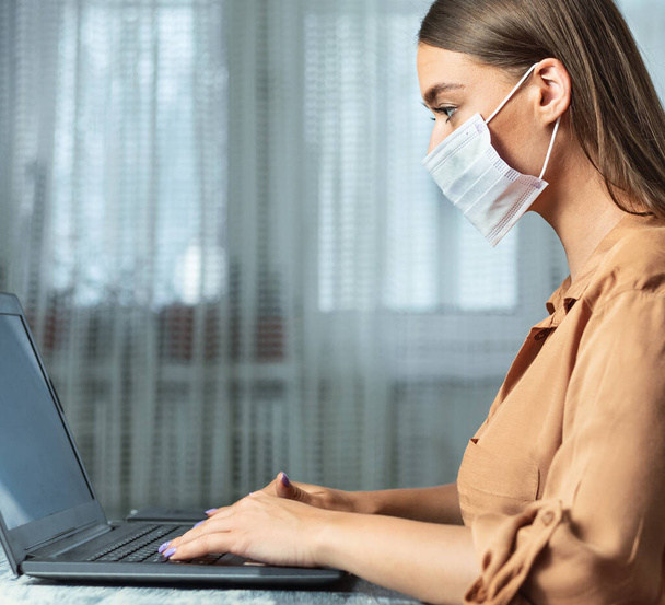Woman wearing face mask and working on laptop, close up - Photo, Image