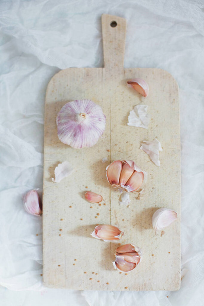 Dientes de ajo en una tabla de cortar de madera sobre un fondo blanco
 - Foto, Imagen