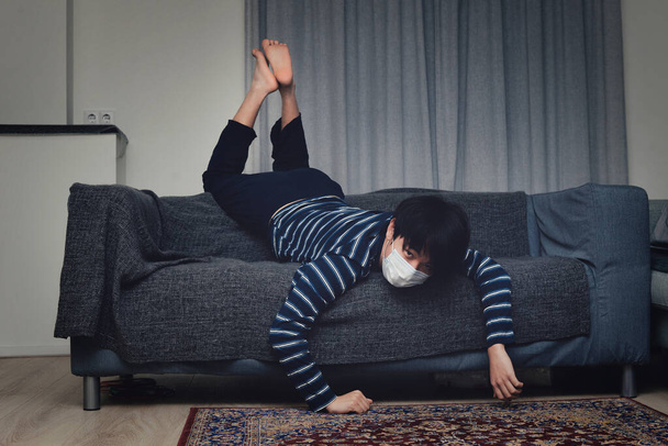 Niño asiático joven que lleva una máscara bucal sintiéndose aburrido en casa (cuarentena concepto en casa
) - Foto, imagen