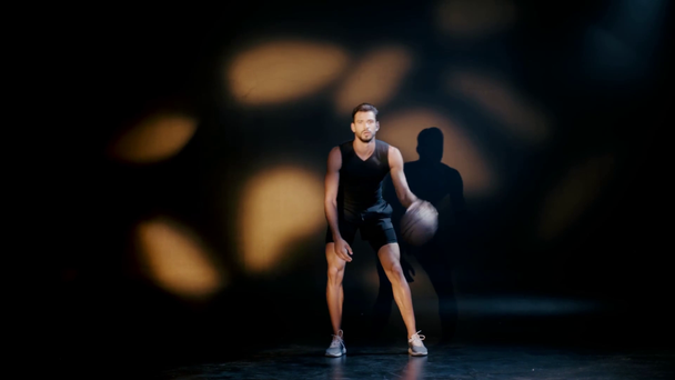 Handsome sportsman training with ball on dark background - Footage, Video