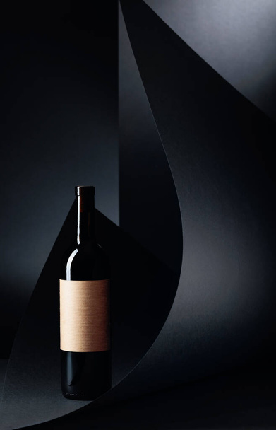Eine Flasche Rotwein mit leerem Papieretikett auf schwarzem Hintergrund. Kopierraum. - Foto, Bild