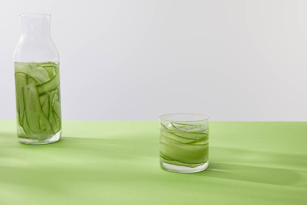 Bottle and glass with drink made of sliced cucumbers on green surface isolated on grey - Fotoğraf, Görsel