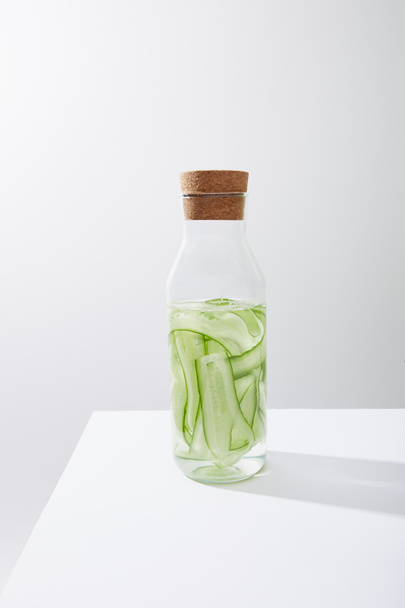 Скляна пляшка з пробкою і напоєм з нарізаних огірків ізольовані на сірому
 - Фото, зображення