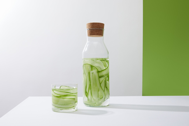 Bottle with cork and glass with drink made of sliced cucumbers on grey and green background - Fotografie, Obrázek