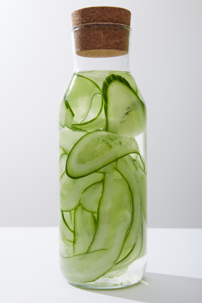 İçi su dolu cam şişe ve gri üzerinde izole edilmiş salatalıklar. - Fotoğraf, Görsel