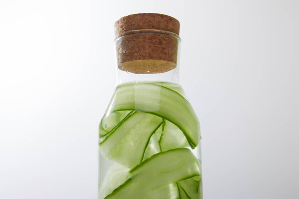 Close up view of glass bottle with cork filled with water and sliced cucumbers on grey background - Foto, Bild